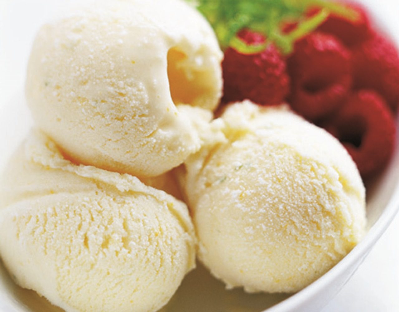 A picture of 3 scoops of ice-cream in a bowl with some raspberries