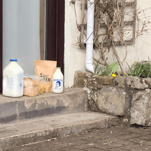 Picture of Milk, Eggs, Bread and Coffee sitting on a doorstep.